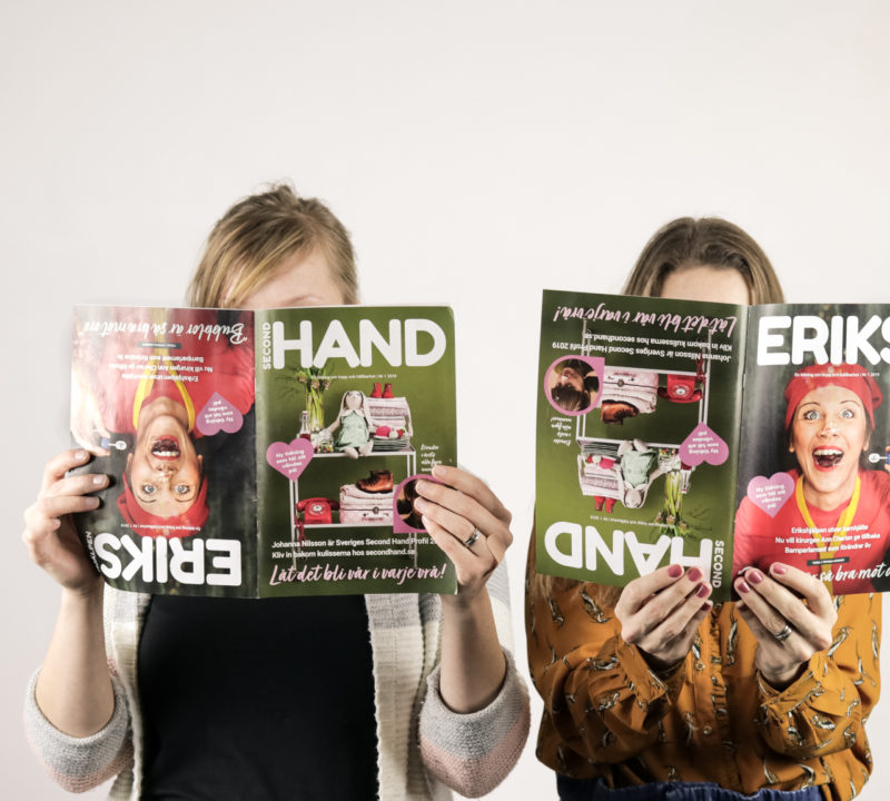 Två personer håller Erikshjälpens tidning framför sina ansikten. Tidningen går att läsa från två olika håll, och därför håller de tidningen på olika håll.