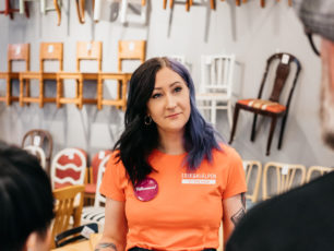 En volontär i Erikshjälpen Second Hand står framför en vägg med stolar och pratar med kunder