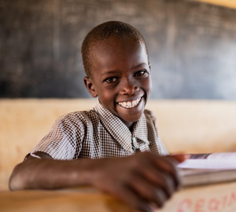 En pojke i skolmiljö ler mot kameran