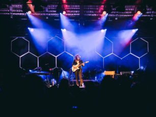Lila ljus lyser fokuserat på Terese Fredenvall som står på scen med sin gitarr.