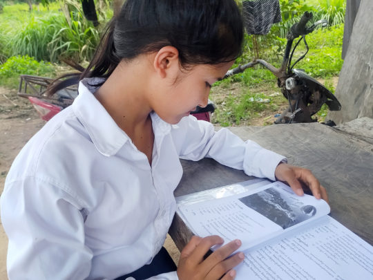 Soeum, en flicka från Kambodja, sitter och läser vid ett bord. Hon syns i profil.