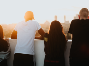 Fyra ungdomar lutar sig mot en kant och blickar ut över en stad.