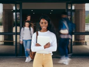 En ung glad kvinna står utanför en gymnasieskola